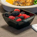 A Dinex black SAN plastic bowl filled with raspberries and blackberries on a table