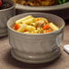 A close up of a Dinex Turnbury latte bowl filled with pasta, vegetables, and broth.