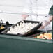A person in a chef's uniform holding a tray of food in a Carlisle portable salad bar.