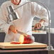 An Avantco stainless steel heat lamp warming a piece of meat on a cutting board.
