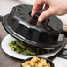 A hand using a black Dinex convection dome to cover a plate of food.