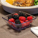 A Dinex clear plastic bowl filled with raspberries and blackberries next to a plate of food.