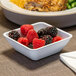 A Dinex white SAN plastic bowl filled with raspberries and blackberries next to a plate of food.