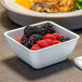 A table with a plate of food and a white Dinex square bowl filled with raspberries and blackberries.