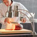 A man in a white coat using an Avantco stainless steel dual arm heat lamp to cut a piece of meat.
