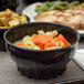 A black Dinex convection bowl with soup, carrots, and noodles.