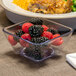 A Dinex clear plastic bowl filled with raspberries and blackberries on a table.