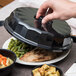 A person's hand opening a Dinex Tropez Onyx convection dome to reveal food on a plate.