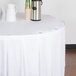A white table with a white tablecloth and Snap Drape TV clear plastic table skirt clips with a white jug on it.