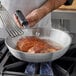 A person cooking meat in a Choice aluminum fry pan on a stove.