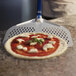 A pizza being placed in an oven using a blue square pizza peel with a white handle.