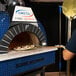 A man using a GI Metal square perforated pizza peel to put a pizza in a stone oven.