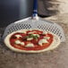 A close up of a pizza being prepared with a blue and white perforated spatula.