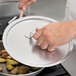 A person holding a Vollrath Wear-Ever aluminum pan cover over potatoes cooking on a stove.