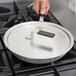 A hand using a black Torogard handle to lift a Vollrath aluminum pan lid off a pan on a stove.