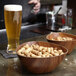 A triangular faux wood bowl with a bowl of peanuts and a glass of beer.