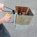 A man holding an Outset Collapsible Briquette Charcoal Chimney Starter box with a yellow handle.