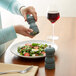 A person using an Acopa steel blue wooden pepper mill to salt a salad.
