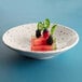 A round chocolate chip melamine bowl filled with watermelon and berries on a blue surface.