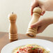 A person using an Acopa wooden pepper mill to grind pepper onto a plate of spaghetti.