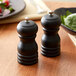 Two Acopa matte black wooden pepper mills on a table.