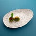An Elite Global Solutions chocolate chip oval melamine plate with two small green fruits on it.