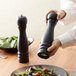 A person using a black Acopa wooden pepper mill to grind pepper over a salad.