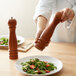 A person using an Acopa brown wooden pepper mill to season a salad.