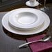 A white Villeroy & Boch deep porcelain plate with a spoon on a table.
