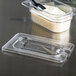 A clear Cambro plastic container lid with a spoon notch.