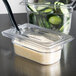 A Cambro clear plastic food pan lid with a spoon notch in a container of cheese and cucumbers.