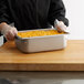 A person in gloves holding a Vollrath stainless steel hotel pan of macaroni and cheese.