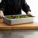 A chef holding a Vollrath stainless steel hotel pan filled with salad.