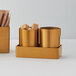 An American Metalcraft gold satin stainless steel round sugar packet holder filled with brown sugar cubes.