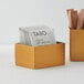 An American Metalcraft gold stainless steel rectangular sugar caddy holding packets of tea.