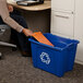 A person putting paper in a blue Rubbermaid recycling bin.