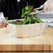 A hand in a plastic glove using tongs to serve salad in a Western Plastics foil container.