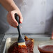 A hand using an OXO black silicone bristle pastry brush to spread sauce on meat.