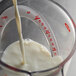 A clear plastic OXO measuring cup filled with milk being poured