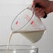 A hand pouring milk into an OXO clear plastic measuring cup.