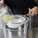 A person pouring liquid through a Tablecraft fine tin mesh strainer.