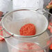 A person using a Tablecraft fine tin mesh strainer to sift ground meat into a bowl.
