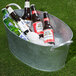 A Tablecraft galvanized steel oval beverage tub filled with beer bottles and ice.
