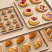 A Baker's Mark gold rimmed aluminum bun tray with pastries on a table.