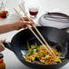 A person using Town bamboo chopsticks to stir noodles in a wok.