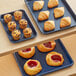 A Baker's Mark dark blue wire rim aluminum sheet pan with pastries and muffins on it on a table.