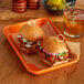 A Baker's Mark orange wire-in-rim aluminum sheet tray with pulled pork sandwiches and a glass of lemonade.