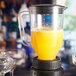 A Waring blender with yellow liquid in it on a table in a juice bar.