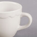 A close-up of a CAC ivory espresso cup with a scalloped edge and a white handle.
