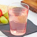 A Fineline Savvi Serve tall clear plastic tumbler with pink liquid and grapes on a table.